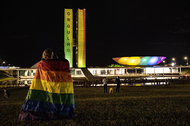Prédio do Congresso Nacional com as cores da comunidade LGBT e um casal com bandeira LGBT