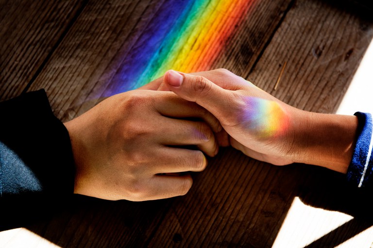 mãos com prisma de luz que remete à bandeira LGBTQIA+